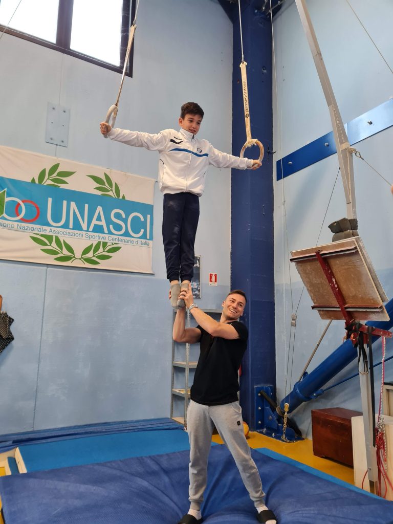 Marco Lodadio aiuta un giovane ginnasta agli anelli